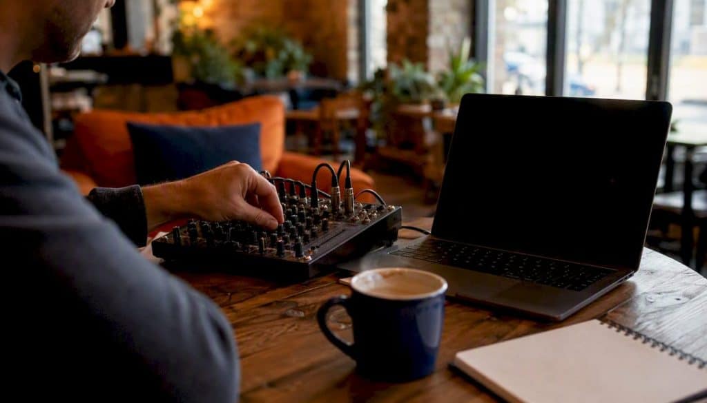 Hand adjusting mixer knobs beside laptop on desk