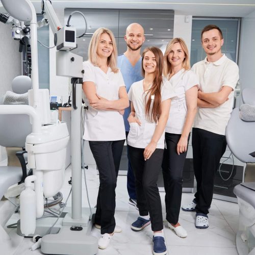 Team of professional dentists and assistants looking at camera and smiling while posing in modern dental office. Dream team. Dentistry and medicine concept.